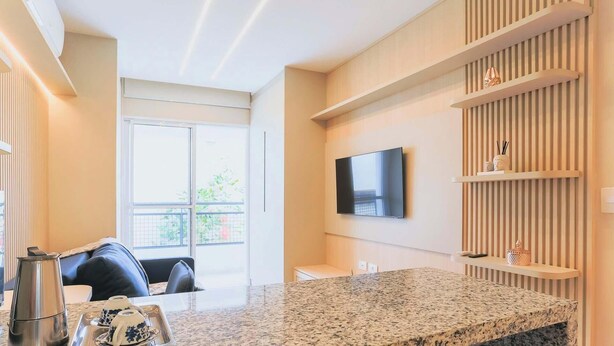 A modern kitchen with a granite countertop, a flat-screen TV mounted on the wall, and a balcony with a view.