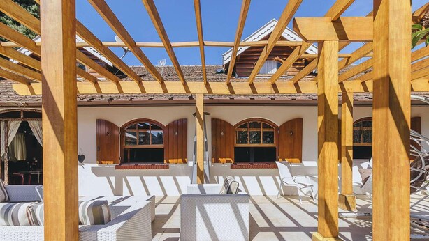 Un espacio de estar al aire libre techado, con vigas de madera y sillas blancas acolchadas.