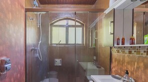 Ein Badezimmer mit Glastür, Fenster, Waschbecken und Toilettenartikeln auf der Ablagefläche.