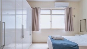 A modern hotel room with a large wardrobe, a bed with a blue bedspread, and a window with curtains.