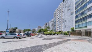 A modern urban street with a parking lot, lined with multi-story buildings featuring balconies and a mix of glass and metal facades.