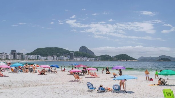 A beach with numerous colorful umbrellas, a sandy shore, and a cityscape in the background.