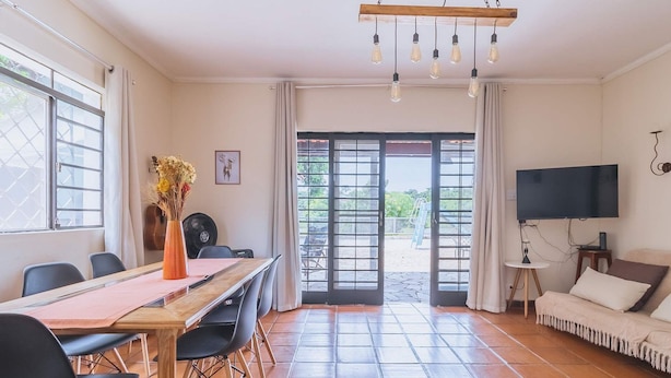 Une pièce comprenant une table à manger, des chaises, un téléviseur, un canapé et donnant sur l’extérieur grâce à une porte vitrée.