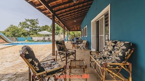 Un patio couvert avec des meubles d’extérieur, une piscine et un mur bleu.