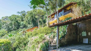 Un edificio de dos pisos con balcón, rodeado de exuberante follaje y árboles.