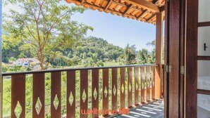 Un balcón con barandilla de madera y vistas a un paisaje verde con árboles y casas.