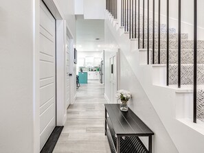 Un couloir moderne avec un escalier, un banc et un vase rempli de fleurs.