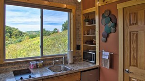 A kitchen with a large window, granite countertop, stainless steel sink, and wooden cabinets.