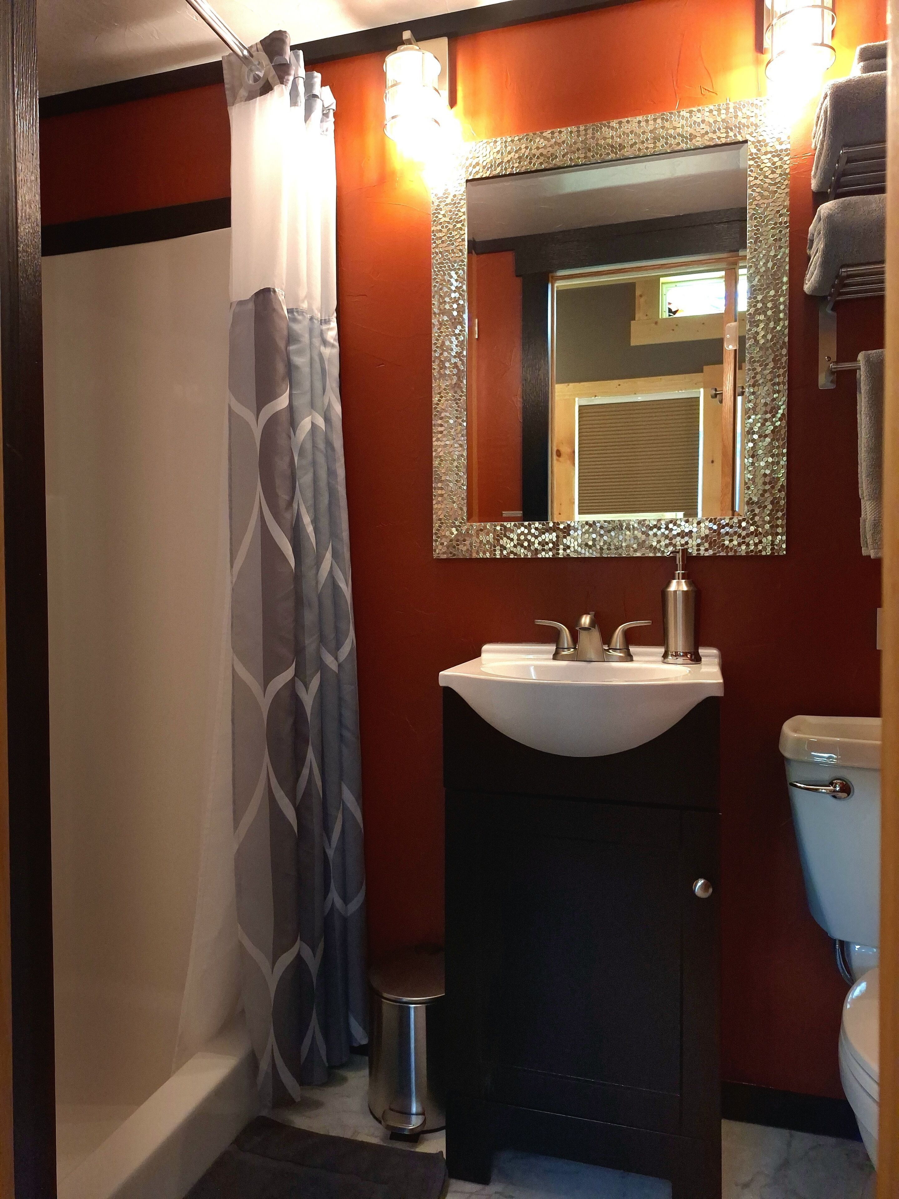 Une salle de bain avec un lavabo blanc, un miroir doté d’un cadre décoratif, des toilettes et un rideau de douche.