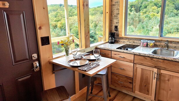 A kitchen with wooden cabinets, a granite countertop, a coffee maker, and a view of the forest.