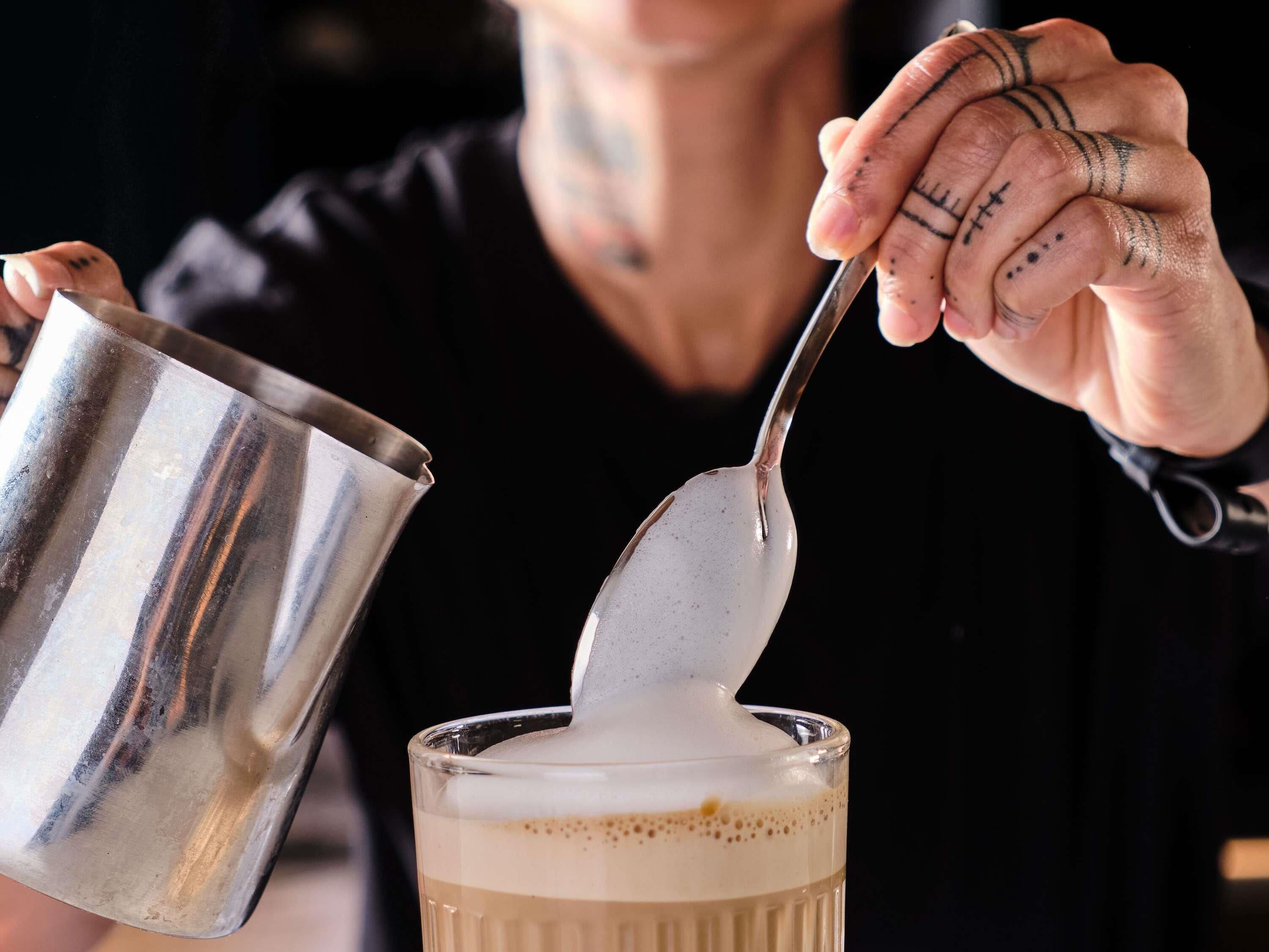 A person pouring a liquid from a metal container into a glass.