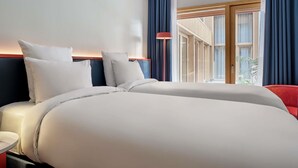 A hotel room with a large bed, a bedside table, a lamp, and a view of the outside through a window with curtains. - TRIBE Paris Pantin (Pantin)