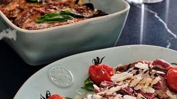 Une assiette de nourriture avec des tomates et du fromage, un plat en arrière-plan et un verre de vin sur une table.