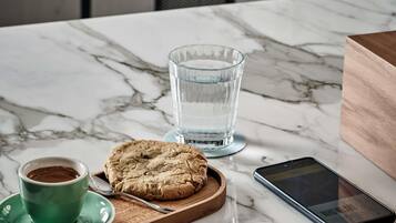 Una mesa de mármol con un vaso de agua, una galleta, una taza de café, un teléfono inteligente y un cuaderno.