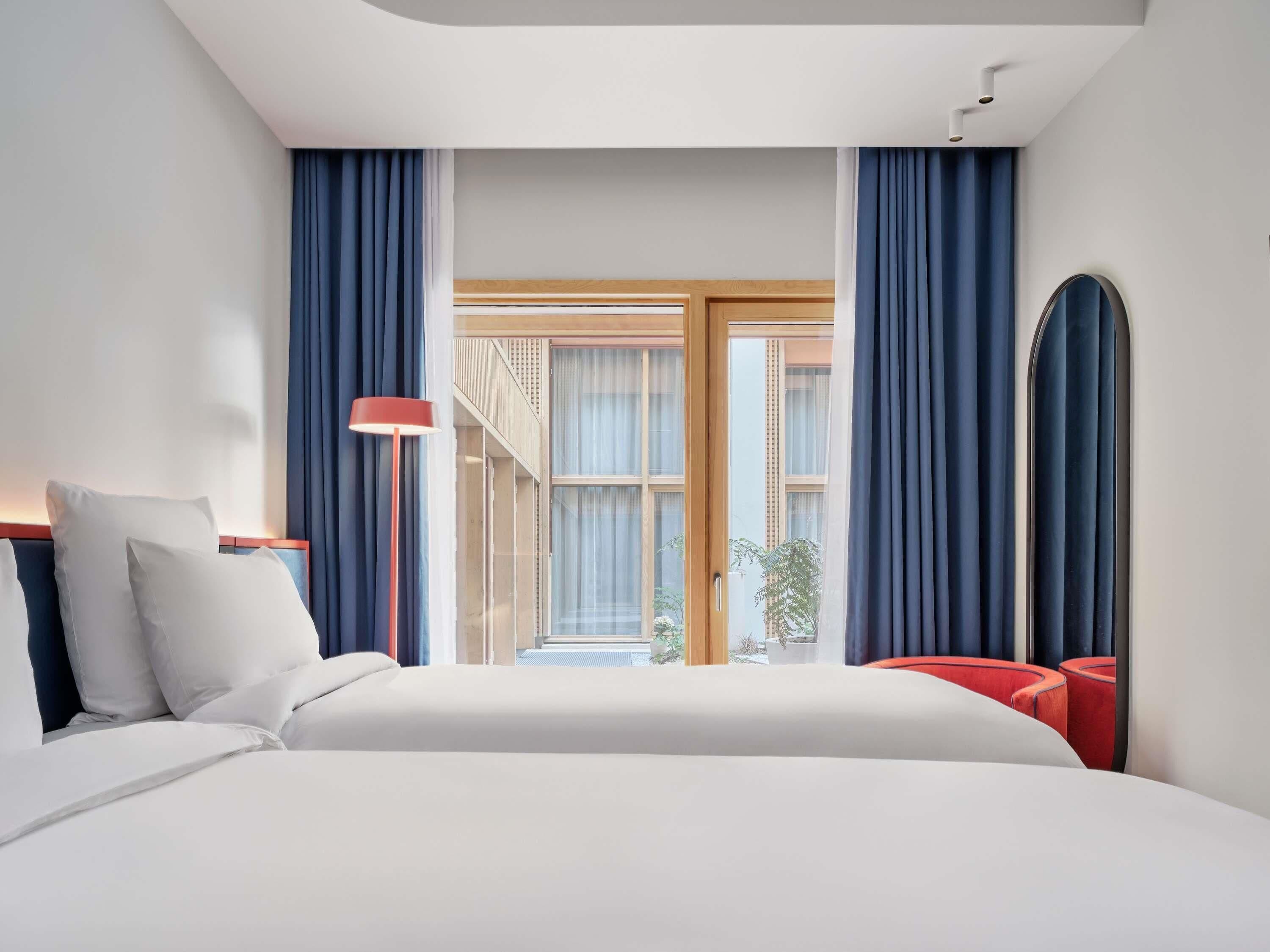 Habitación de hotel moderna con cama, lámpara roja, ventana grande y vistas al exterior.
