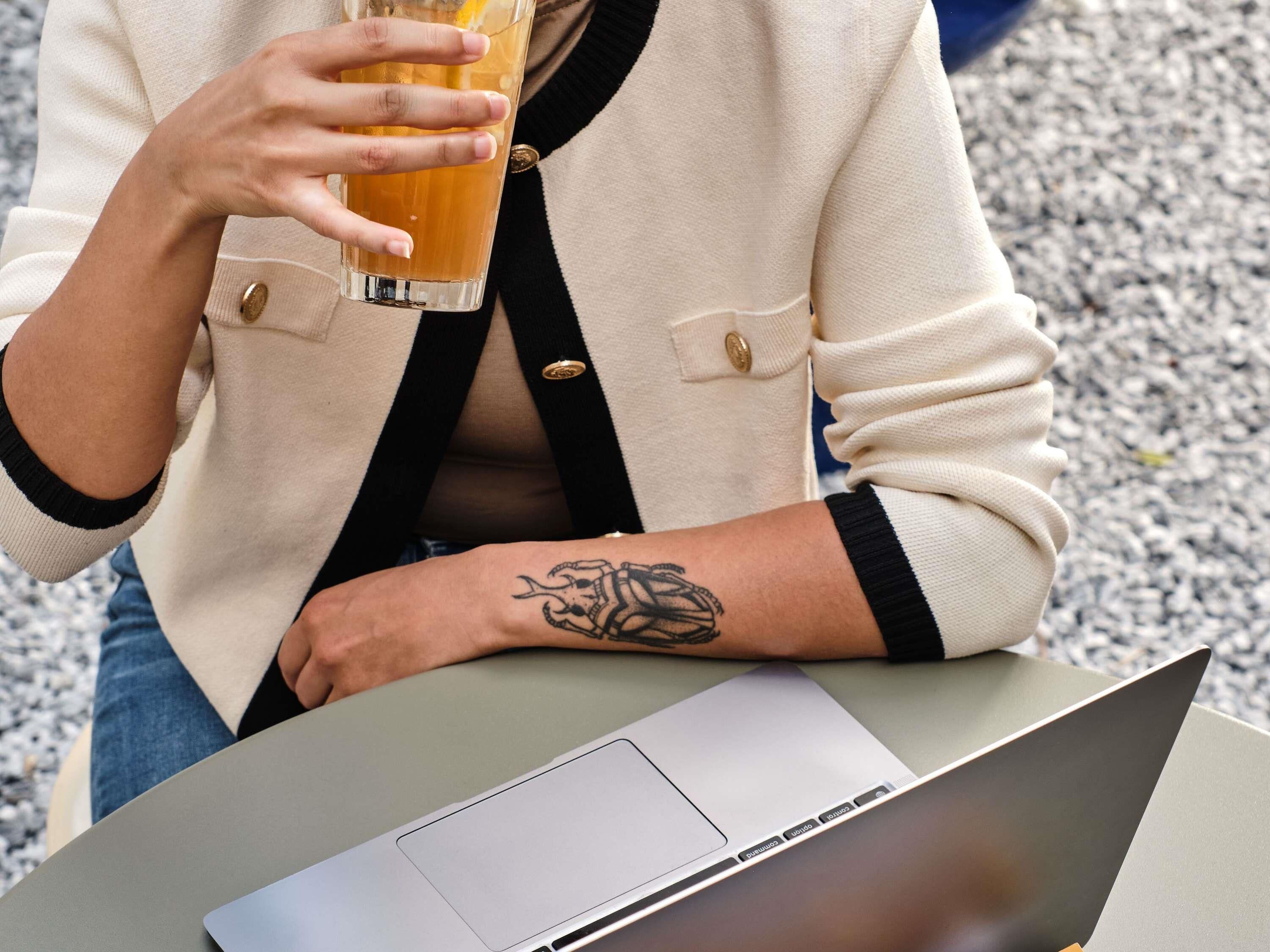 A person sitting at a table with a laptop and holding a glass of amber liquid.