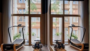 A gym with treadmills, rowing machines, and benches, large windows with a view of buildings and trees. - TRIBE Paris Pantin (Pantin)