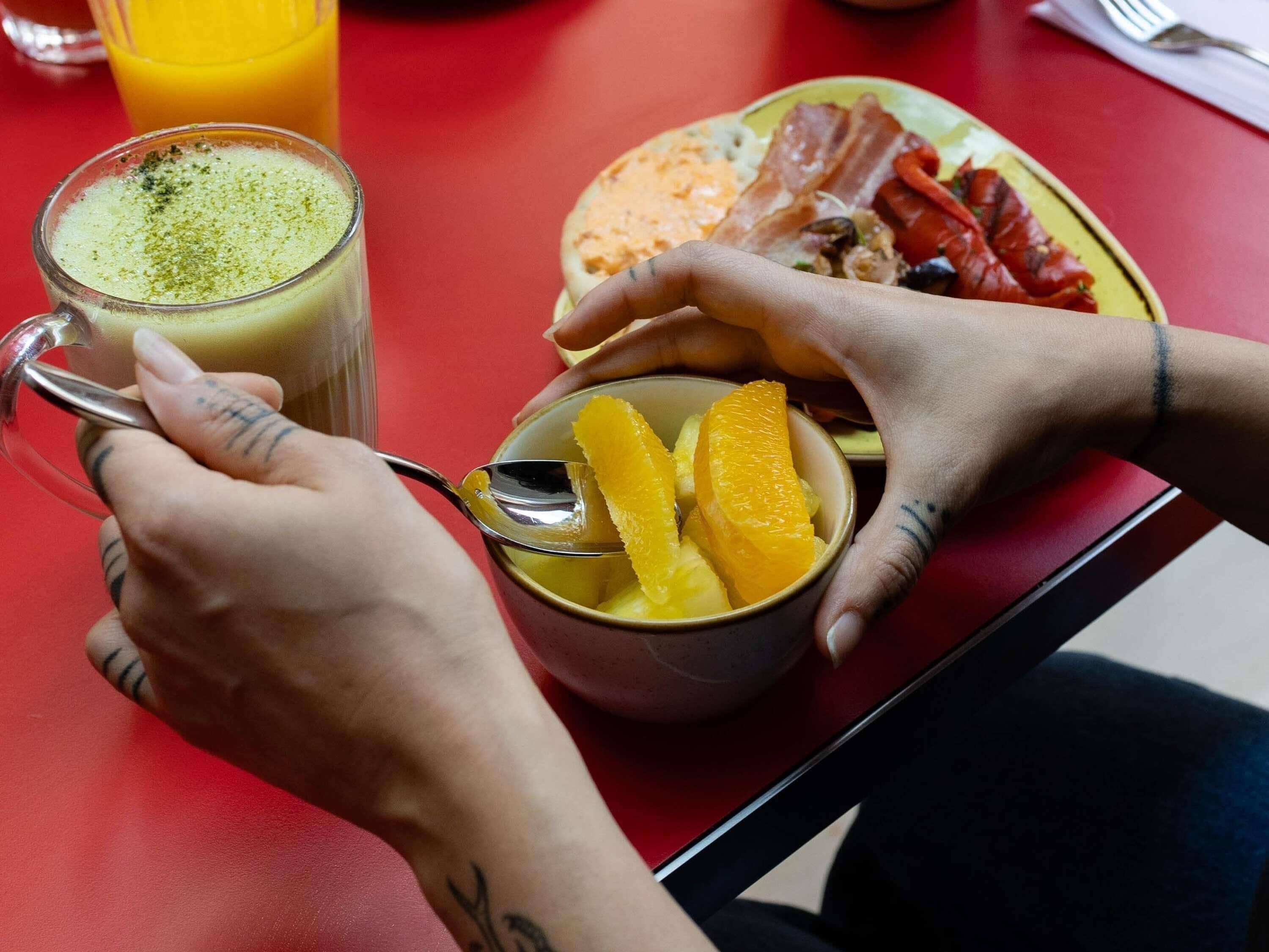 A person eating a meal with a bowl of fruit and a drink on a red table.
