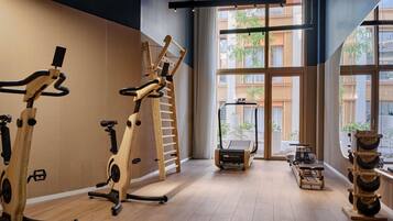 Une salle de sport équipée de matériel d’exercice, dotée de grandes fenêtres et offrant une vue sur les bâtiments environnants.