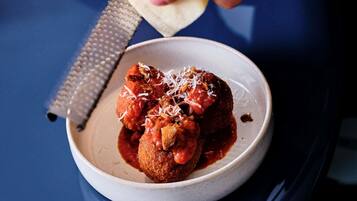 A bowl of meatballs in tomato sauce with grated cheese.