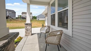 A covered porch with two wicker chairs, a stone pillar, and a view of neighboring houses. - Lunar Haven (Walton)