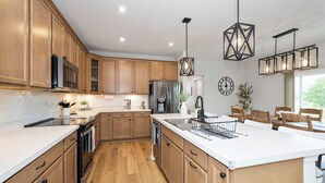 A modern kitchen with wooden cabinets, a large island, stainless steel appliances, and pendant lighting. - Lunar Haven (Walton)
