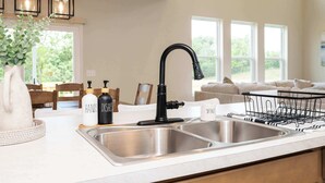 A modern kitchen with a double sink, black faucet, pendant lights, and a dish rack. - Lunar Haven (Walton)
