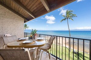 Un balcon avec une table dressée pour deux personnes, donnant sur une plage bordée de palmiers et sur l’océan.