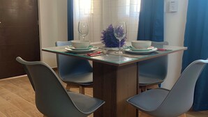 A dining area with a glass-top table, four grey chairs, two bowls, two wine glasses, and a purple plant centerpiece. - Modern and charming apartment with pool Punta Sur (Isla Mujeres)