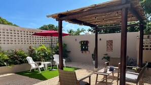 A covered outdoor seating area with chairs and tables, surrounded by a gravel floor and green turf. - Modern and charming apartment with pool Punta Sur (Isla Mujeres)