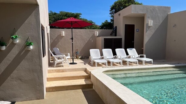 A pool area with white lounge chairs and a red umbrella. - Modern and charming apartment with pool Punta Sur (Isla Mujeres)