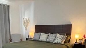 A bedroom with a bed, nightstands, a ceiling fan, and a wall-mounted light fixture. - Modern and charming apartment with pool Punta Sur (Isla Mujeres)