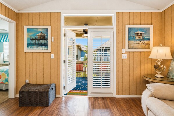A room with wooden paneling, a wicker bench, a door leading outside, and a framed painting on the wall.