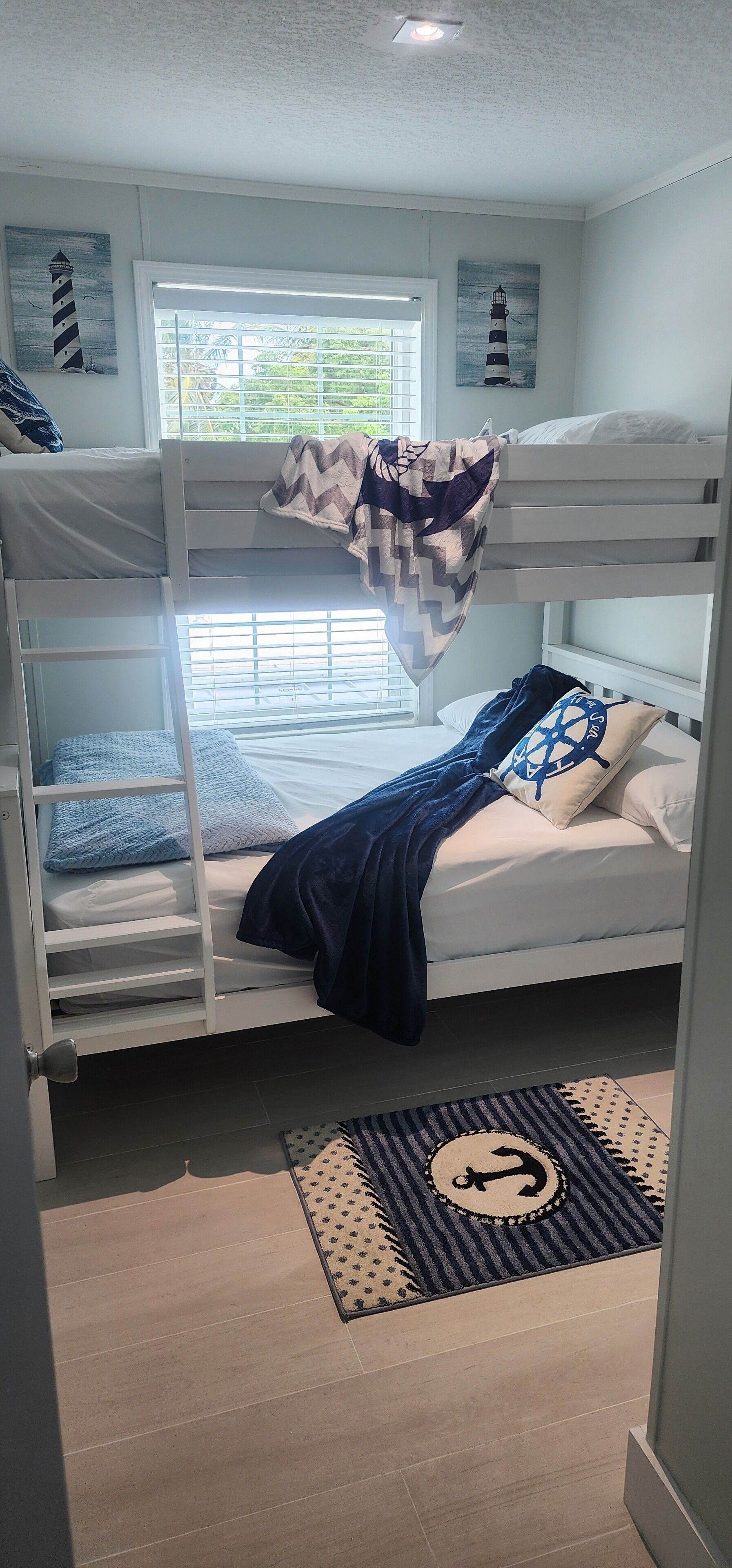 Habitación con literas, un ventanal, un tapete con motivos náuticos y un cuadro de un faro.