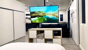 A modern hotel room with a large bed, a flat-screen TV on a wooden stand, and a wardrobe with multiple compartments.