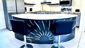 A modern kitchen with a central island, two black bar stools, stainless steel appliances, and a microwave above the counter.