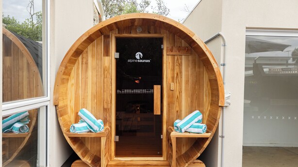 A wooden sauna with a sign reading "alpine saunas" and two benches with towels.