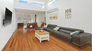 A spacious living room with a wooden coffee table, a grey sofa, and a billiards table in the background.