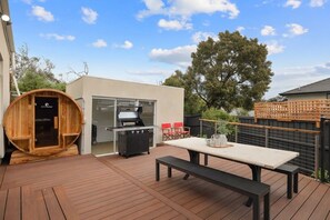 A wooden deck with a barbecue grill, a wooden sauna, and a table with chairs. - Currawong Paradise Cowes (Cowes)