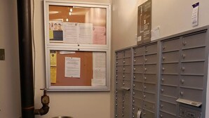 A hallway with a bulletin board, a trash can, and a row of mailboxes. - Live Close to Everything! (Oakland)