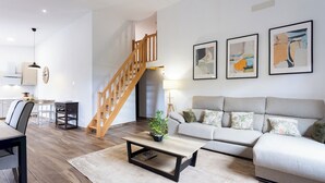 Una sala de estar moderna con una escalera, un conjunto de sofás, una mesa de centro y un comedor.
