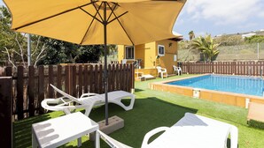 Un patio trasero con piscina, sillas de descanso blancas y un paraguas amarillo.