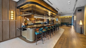 A modern bar area with a long counter, multiple stools, and a variety of bottles and glasses. - 601 RESIDENCES WONDERFUL 1BR UNIT #3203 (Miami)