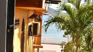 Un sendero estrecho que lleva a un edificio con balcón, rodeado de plantas y vistas al mar.