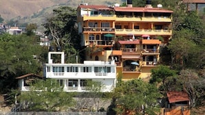 Un edificio de varios pisos con balcones, una estructura blanca al frente y una playa en el fondo.