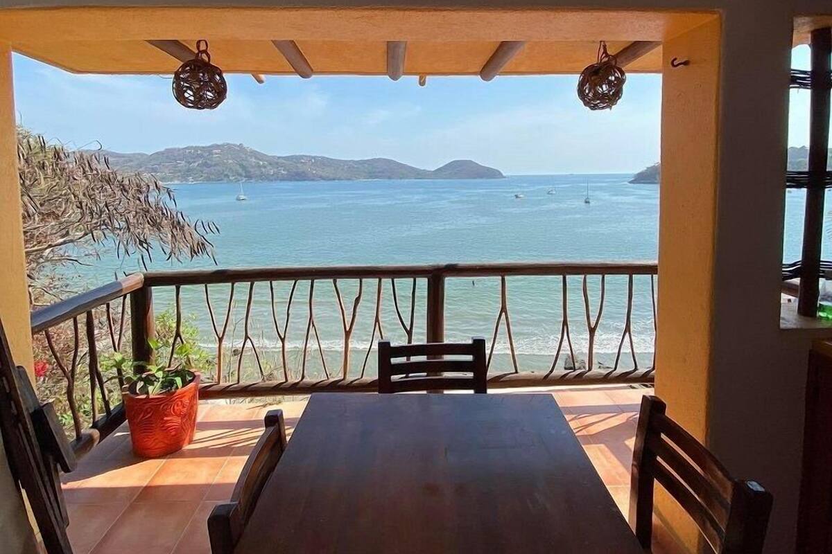 A wooden table and chairs on a balcony with a view of the sea and hills.