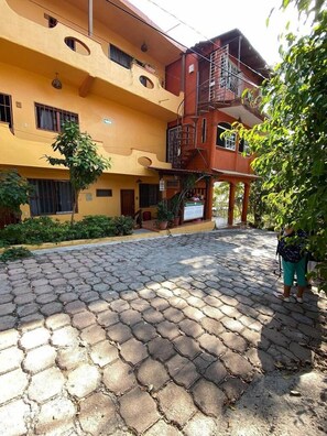Um edifício com fachada amarela, varanda vermelha e pátio de pedra.