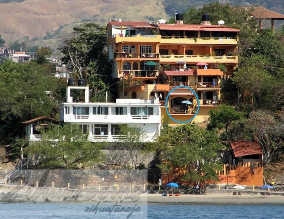 Un edificio a più piani con balconi, una struttura bianca in primo piano e un ombrello blu al centro.