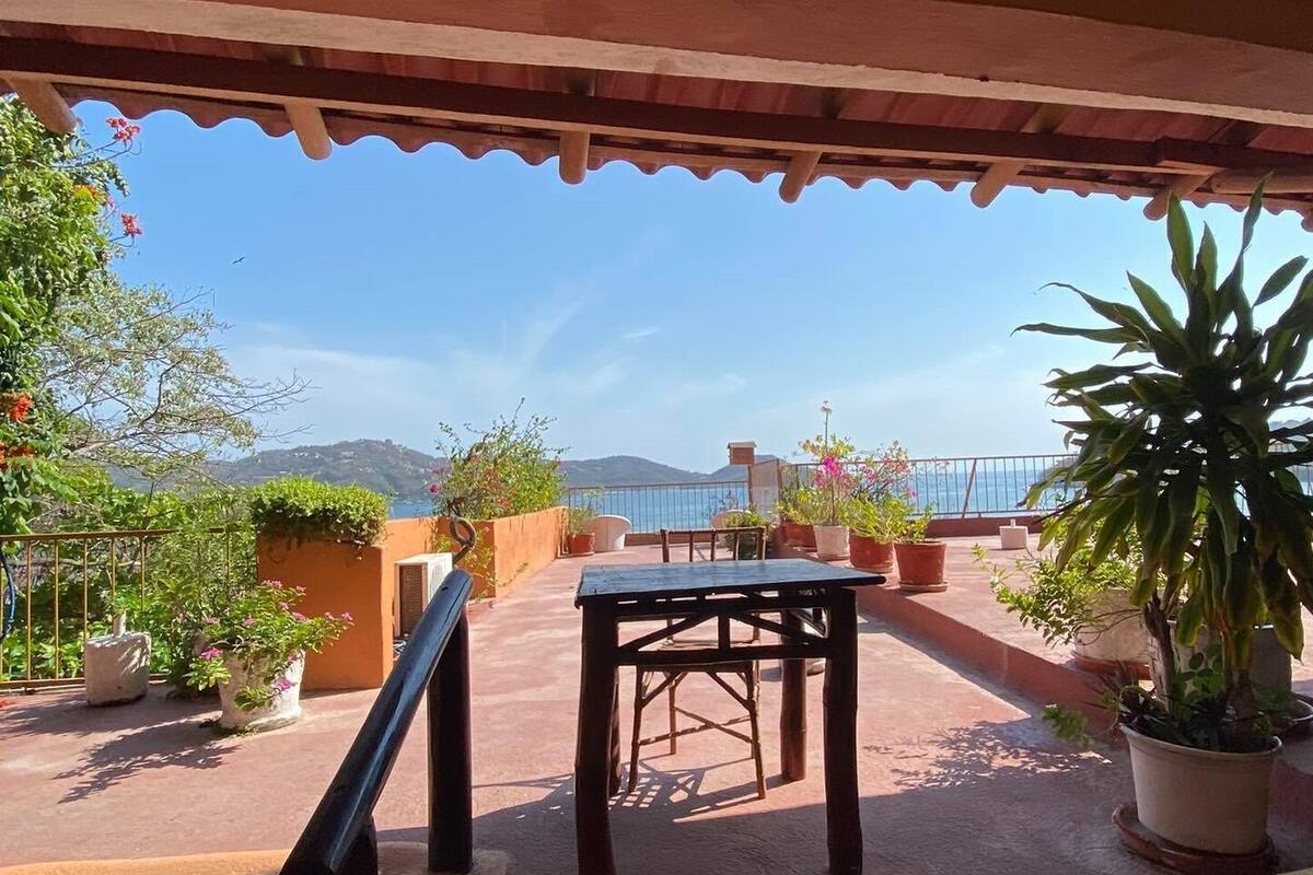 A terrace with a table and chairs, potted plants, and a view of the sea.