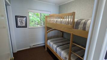 A bunk bed room with a window, a radiator, and a framed picture on the wall.